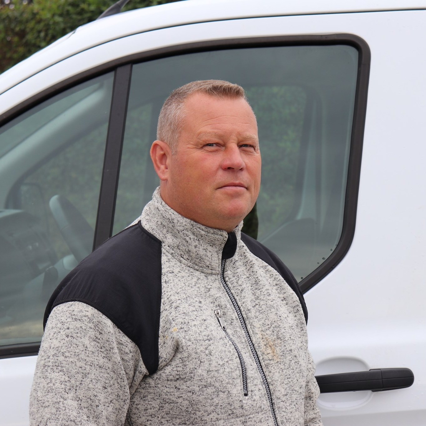 Ejeren af Hersing's Anlæg smiler foran et nyetableret haveanlæg – din lokale, pålidelige anlægsgartner med fokus på kvalitet og god service